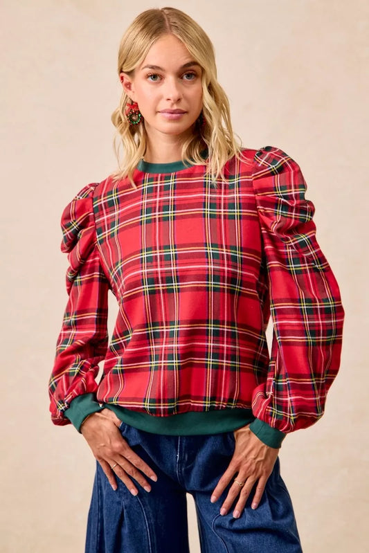 Woman wearing a red plaid blouse with puffed sleeves against a beige background