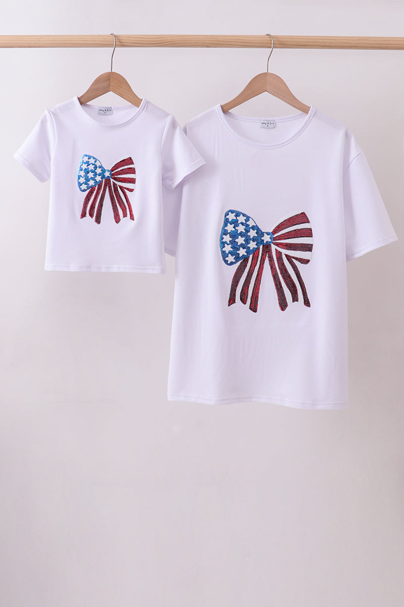 Two white t-shirts with bow designs on a wooden rack against a white background
