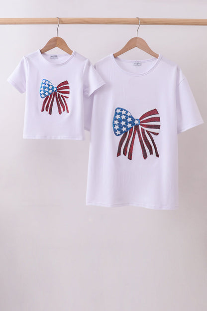 Two white t-shirts with bow designs on a wooden rack against a white background